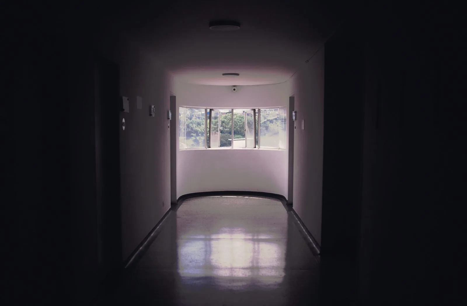 A dim clinical corridor running to one lit curved window.