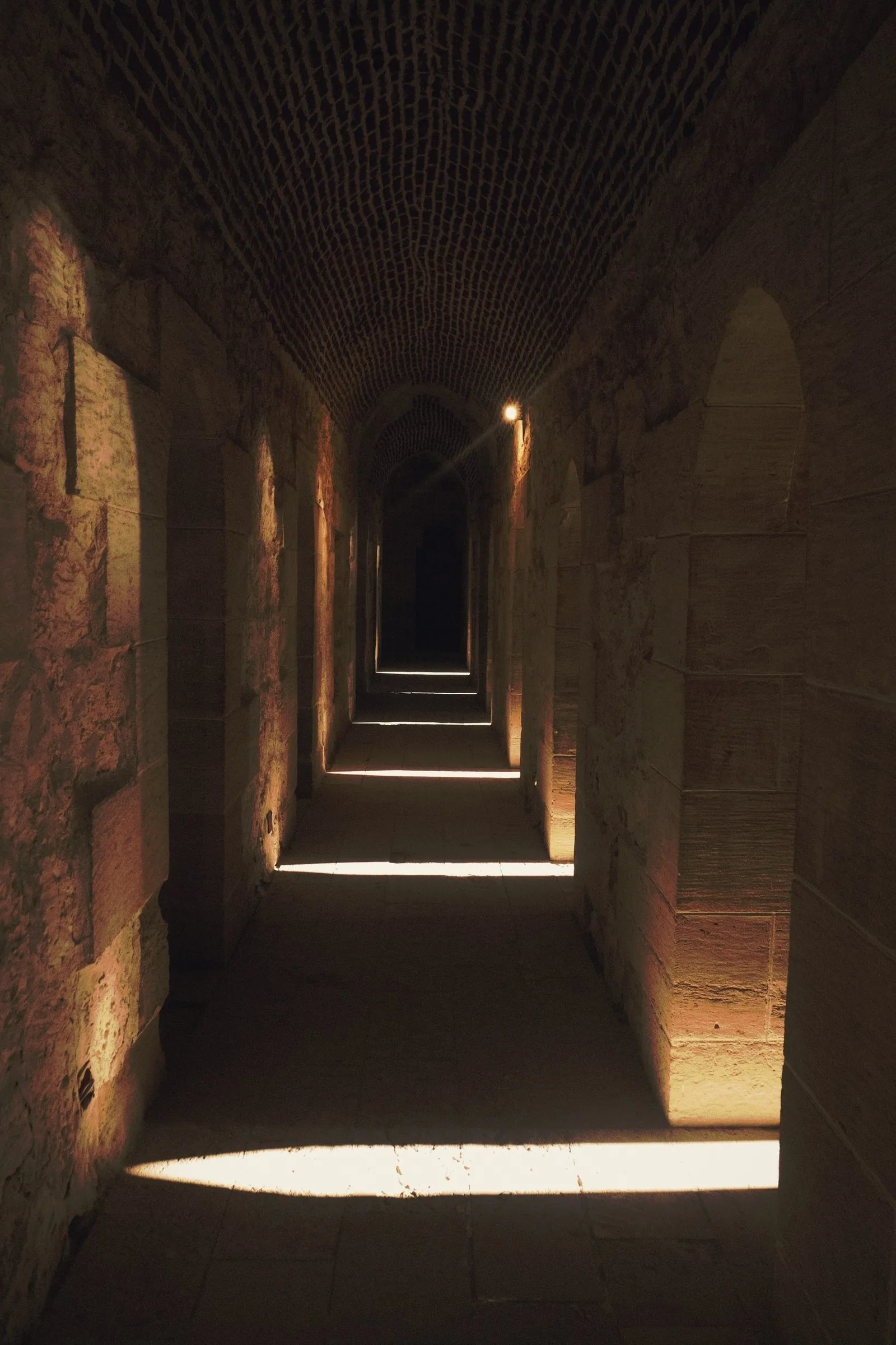 Stone arches receding into the dark, one blade of daylight across them.