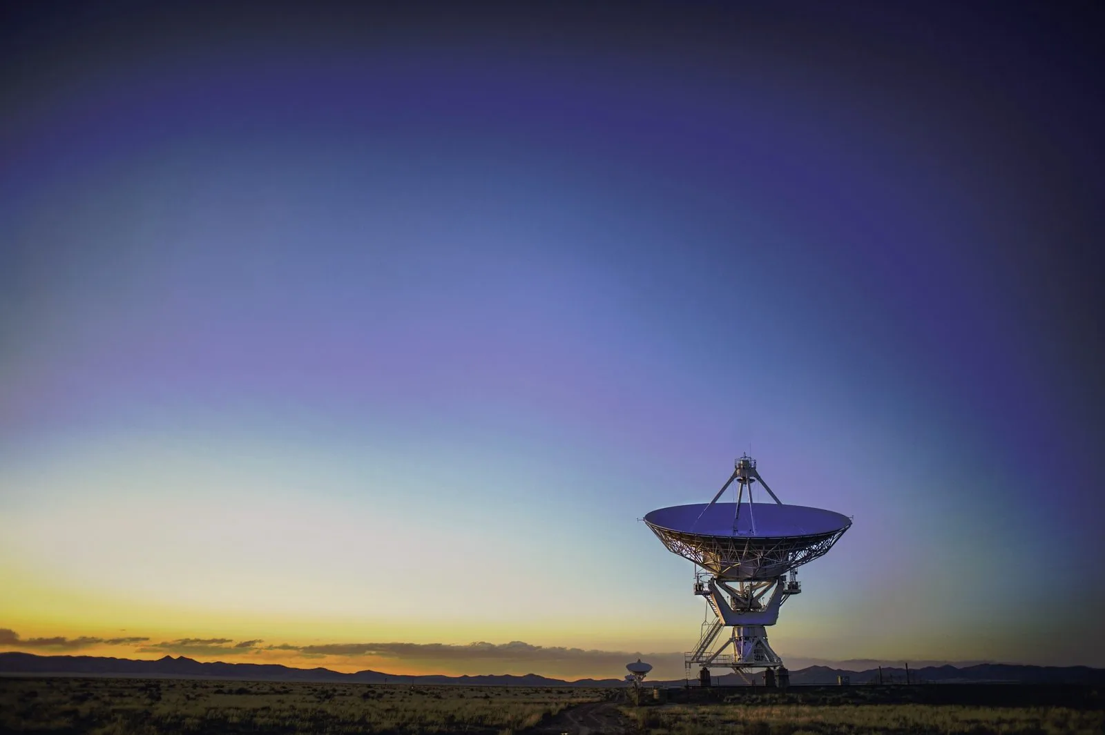 A dish antenna standing on open ground at dusk.