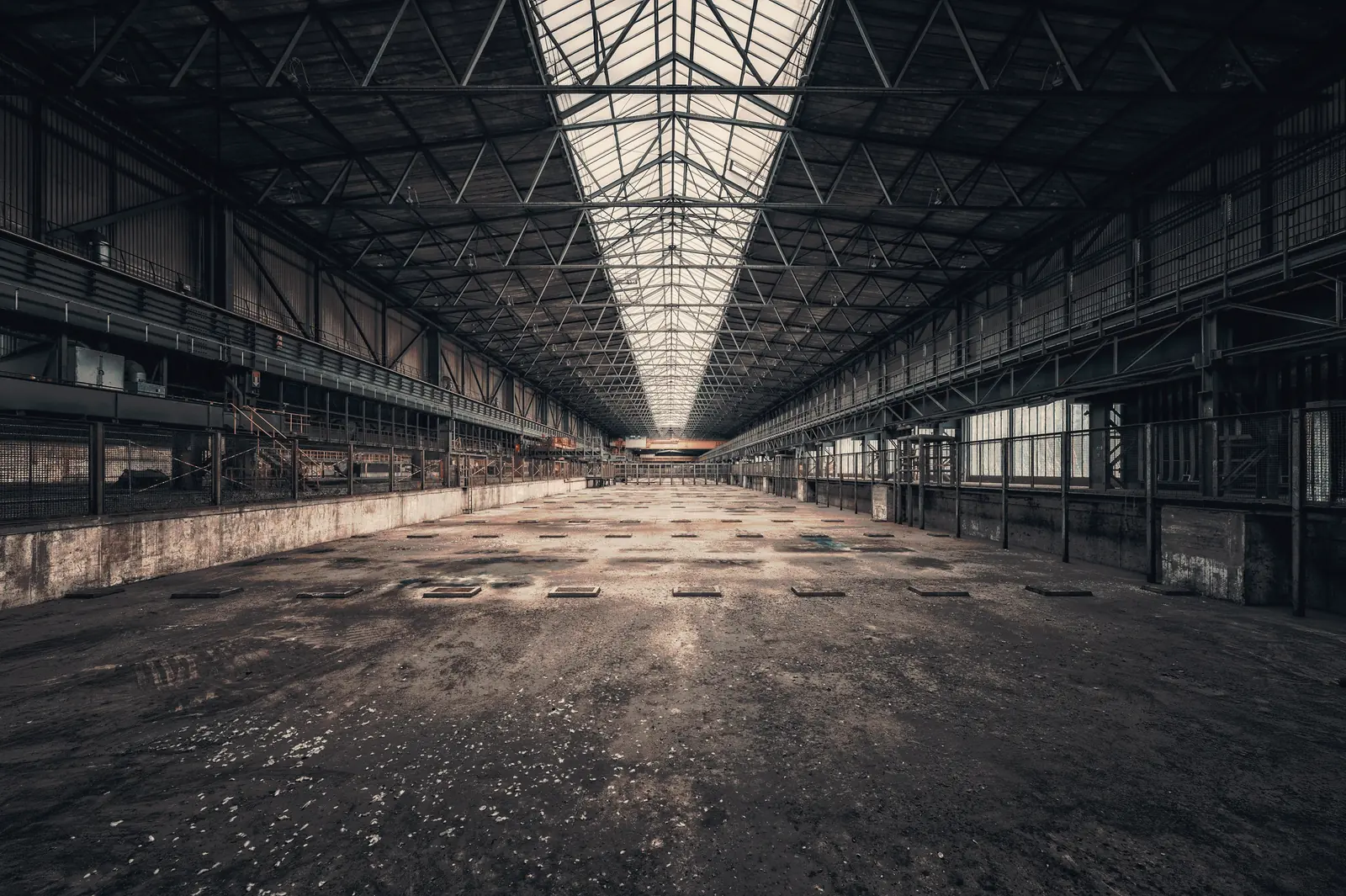 An empty machine hall at dawn, light down the roof ridge from high windows.
