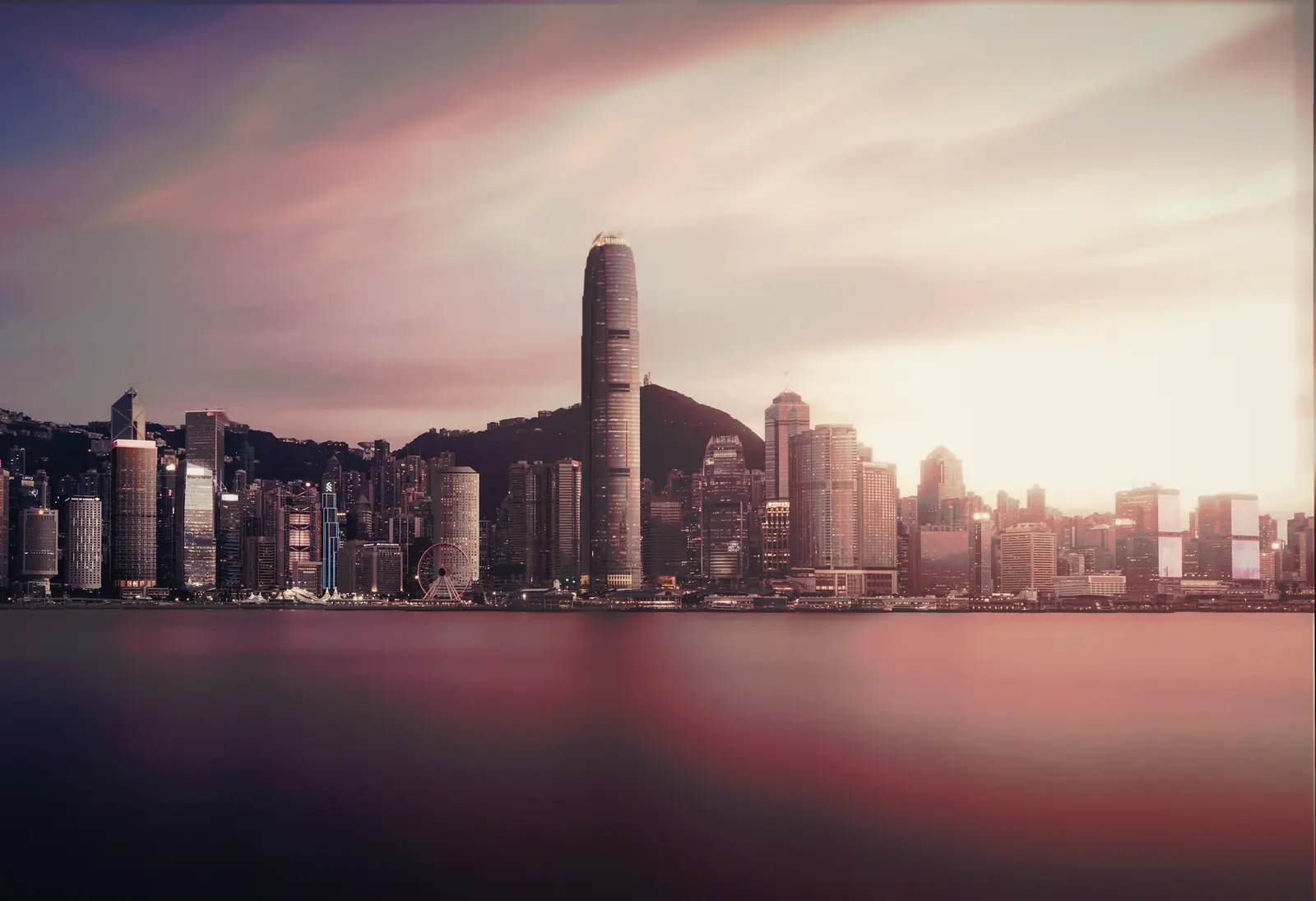 The Hong Kong Island skyline in colour across Victoria Harbour at dusk.