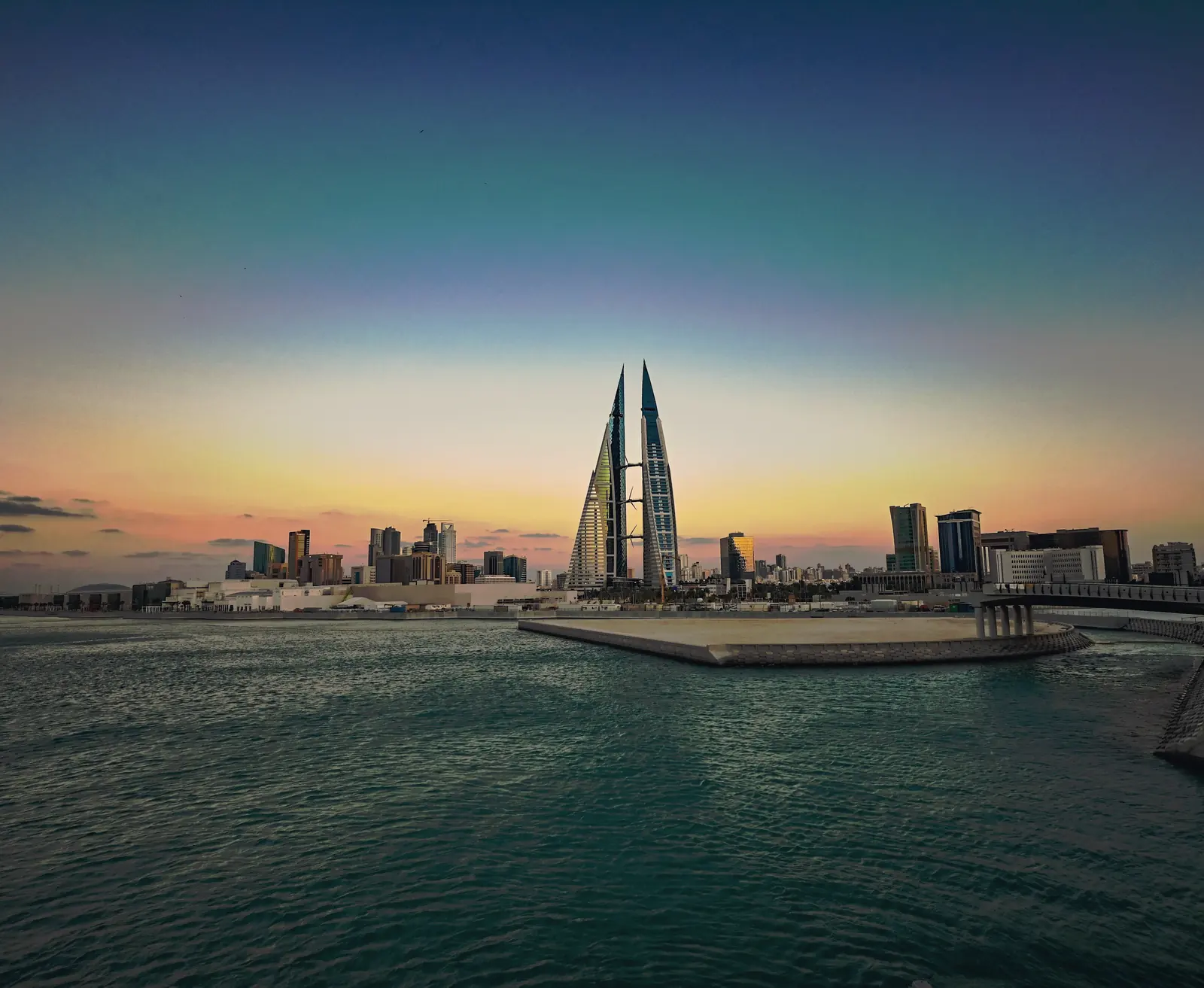 The Bahrain World Trade Center&rsquo;s twin towers across the harbour at dusk, seen from the water.