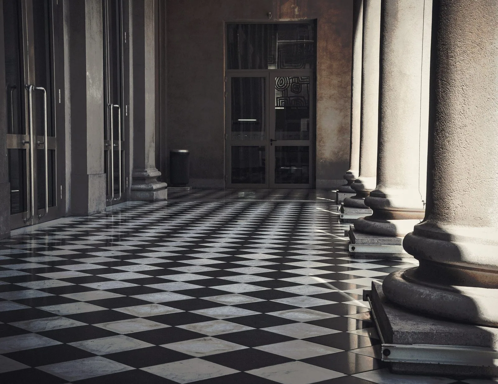 A stone colonnade beside a checkered marble floor, lit from one side.